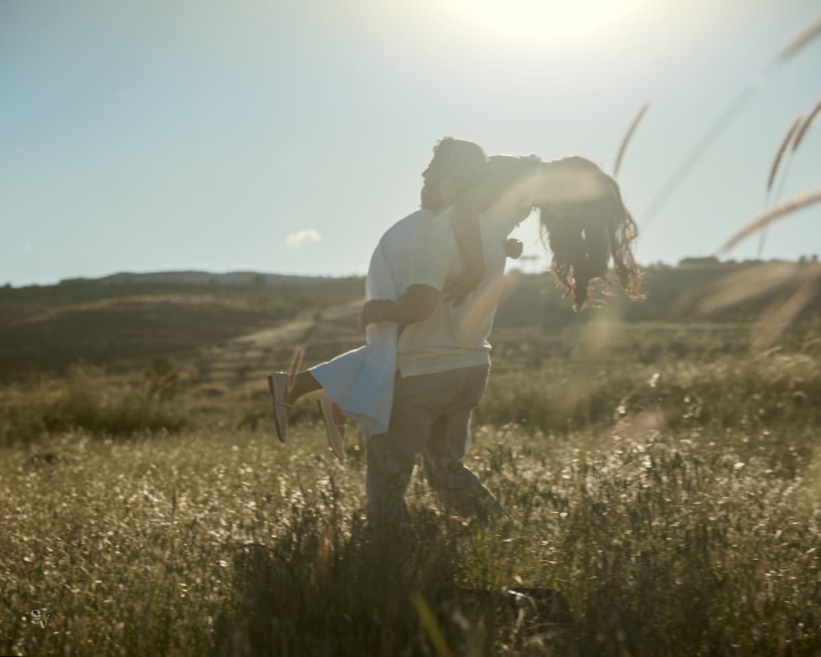 Amir lifting Lynn in a sunlit field with lens flare